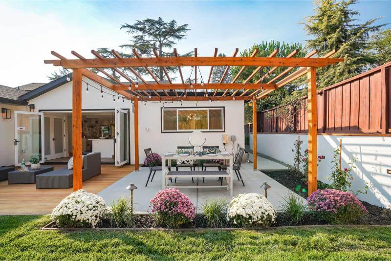 Jardín con una pérgola de madera y muebles de exterior, creando una zona de sombra y descanso. Para Vivir el Verano al Máximo.