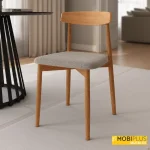 Silla de comedor de estilo nórdico en madera clara con respaldo curvo de madera y asiento tapizado en tejido gris o beige texturizado.