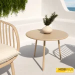 Mesa auxiliar redonda Samoa de 60 cm en acabado arena con florero sobre terraza soleada.