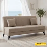 Texto Alt: Sofá cama clic clac modelo Fiji tapizado en tela de color beige en un ambiente mediterráneo frente al mar.