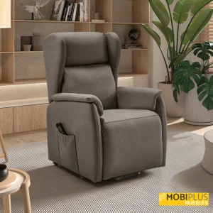 Sillón elevador Vega taupe en un salón contemporáneo con estantería de madera y plantas decorativas.