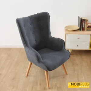 Sillón nórdico Voss en tela gris oscuro en un rincón de lectura con mueble bajo y libros.
